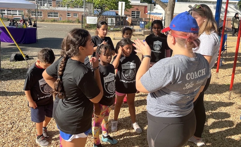 A diverse group of young female soccer players huddle with their coach